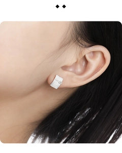 Macro view of rectangular silver earring with brushed texture and small inset diamond