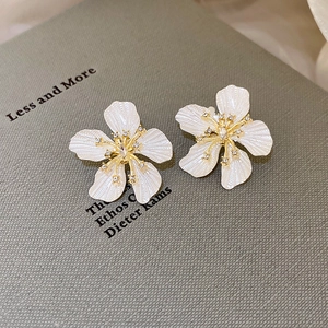 Detail shot of white flower earring with gold stamen and zircon on a textured book