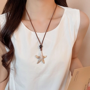 Detail of starfish pendant on brown leather cord worn by model over a white top