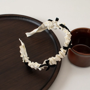 Macro shot of white pleated fabric headband with small black bows on a dark tray