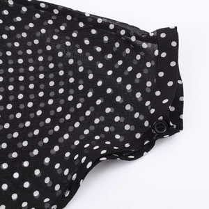 Dettaglio della camicetta nera a pois che mostra la trama del tessuto e il bottone del polsino