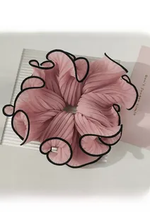 Detail of a large pink pleated organza scrunchie with black trim on a glass surface