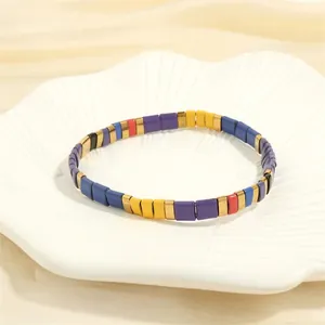 Macro shot of colorful Tila bead bracelet with golden spacers on white shell plate