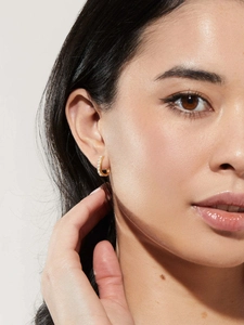 Close-up of model wearing gold U-shaped hoop earrings with faux pearls and micro-pave crystals
