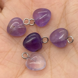 Macro shot of five heart-shaped amethyst pendants with metal loops held in a palm for size