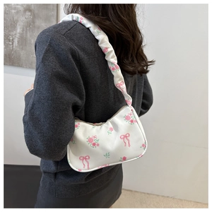 Detailed shoulder strap with pink rose and bow prints on a white leather underarm bag