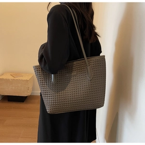 Detail of dark grey woven tote bag with slim shoulder straps worn by model