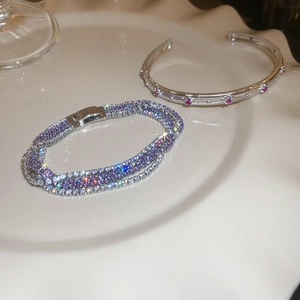 Detail eines mehrreihigen lila Edelsteinarmbandes und Silberreifens mit rosa Kristallen