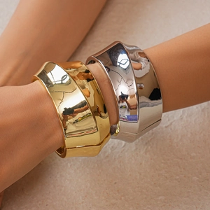 Close-up of polished gold and silver architectural wide open bangles on wrist