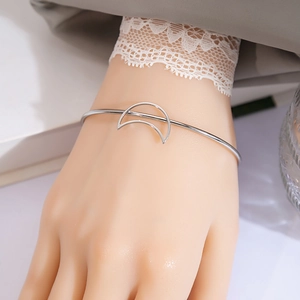 Close-up of a silver crescent moon open bangle worn with lace detail on the sleeve