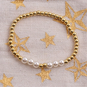 Elegant gold bead and white pearl stretch bracelet displayed on a starry linen fabric background