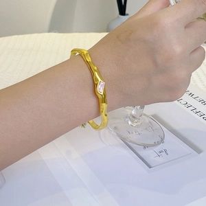 Detail of gold C-shape bangle with hammered texture and rectangular zircon on wrist