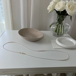 Detailed view of long minimalist pearl necklace on a white table with floral background