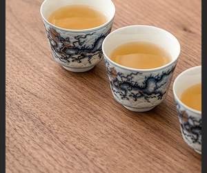 Close-up of ceramic teacups with blue and gold dragon patterns on wooden background