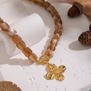 Detail of amber resin beads and golden flower pendant with T-bar clasp on rustic stone