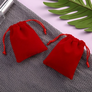 Red velvet drawstring jewelry pouches with soft texture on a grey fabric background