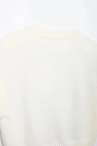 Detailed close-up of the crew neck and soft knit texture of the white sweater vest
