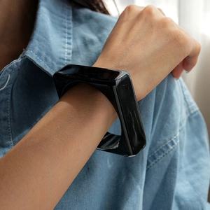 Close-up of a wide square black acrylic bangle worn with a blue denim shirt sleeve