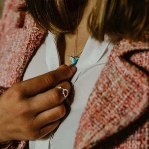 Detail shot of blue enamel hummingbird necklace paired with gold chain on model