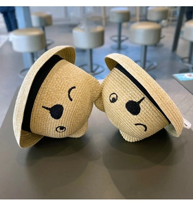 Detail of straw sun hats for toddlers featuring black ribbon and cartoon face embroidery