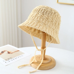 Cappello a secchiello in paglia beige con lacci esposto su un supporto di legno