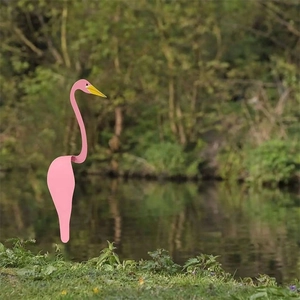 Pink flamingo swirl bird garden ornament standing on a lush green lawn near water