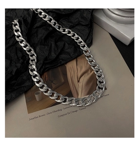 Vue à plat d'un collier grosse chaîne cubaine argentée sur un fond de magazine de mode