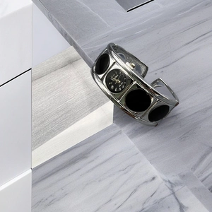 Detail of silver bangle watch with hollow ring strap and black dial on marble surface