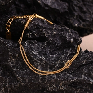 Detail of 18K gold double-layer snake chain bracelet featuring a central knot on black rock