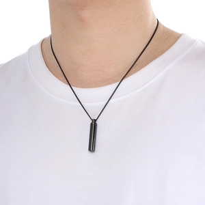 Detail of a black cylindrical pendant necklace shown on a model wearing a white t-shirt
