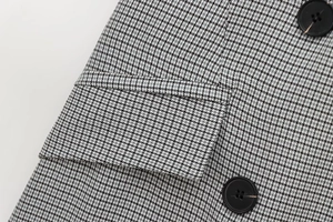 Close-up of black and white houndstooth fabric with buttons and pocket flap detail