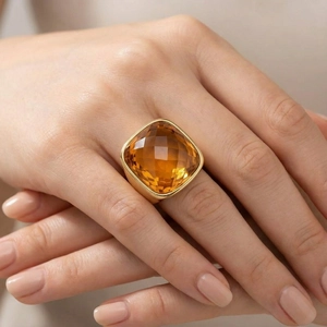 Macro shot of cushion-cut amber glass ring in golden setting on woman's finger