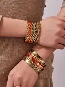 Close-up of layered stainless steel gold bracelets with colorful enamel checkered patterns