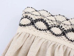 Détail de la jupe en lin beige avec bordure en dentelle noire et blanche et plis