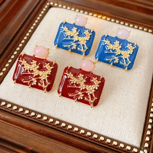 Close-up of vintage enamel earrings with gold branches and pink gems on wood
