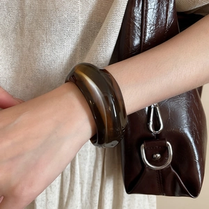 Close-up of translucent amber acrylic wide cuff bracelet worn on wrist for fashion