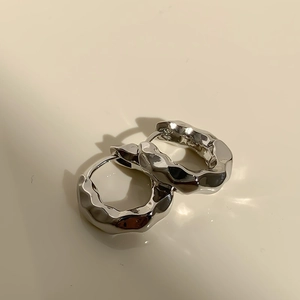 Macro detail of silver irregular wavy hoop earrings with high-polish metallic finish