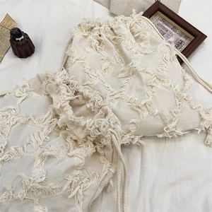 Close-up of cream canvas drawstring bag featuring textured tassel diamond pattern details