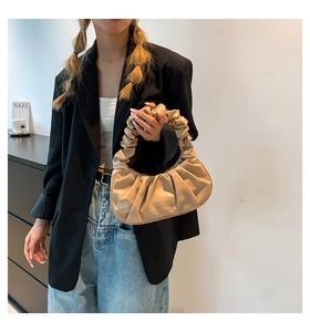 Close-up of beige pleated cloud bag held by a model in a black blazer and jeans