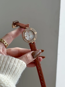 Detail of gold watch case with crystal bezel and brown quilted leather strap