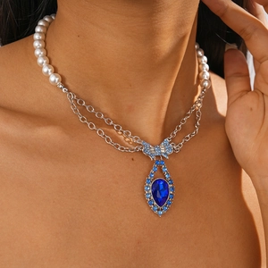 Close-up of vintage pearl necklace featuring a large blue teardrop gemstone and bow knot