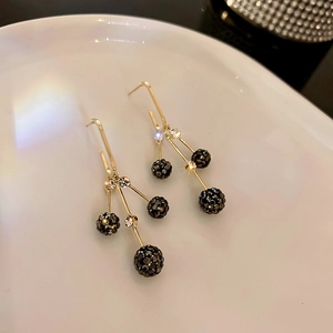Détail de boucles d'oreilles pendantes dorées avec trois boules de strass noirs élégantes