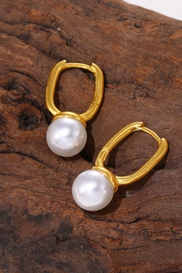 Macro detail of glossy round pearls on 18k gold plated tassel earrings over wood background