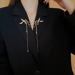 Dettaglio di una spilla dorata con uccelli in volo e nappe di perle su un blazer nero