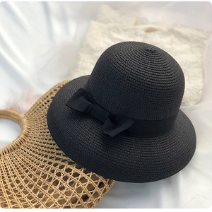 Detail of black straw sun hat with ribbon bow on white fabric with accessories