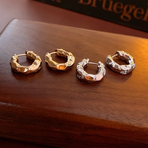 Macro detail of textured gold and silver irregular hammered hoops on dark wood
