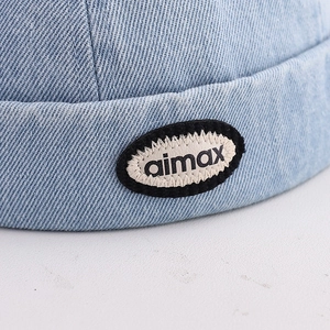 Macro shot of embroidered logo patch on light blue denim brimless dockman cap