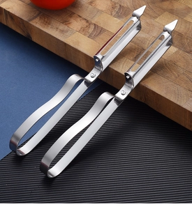 Detailed macro view of two stainless steel vegetable peelers with serrated blades on a wood board