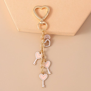 Detail of golden heart-shaped clasp with pink enamel heart and key charms on a keychain