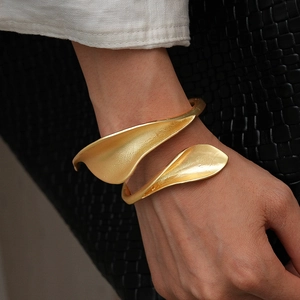 Detail of matte gold leaf-shaped wrap bracelet on model's wrist with brushed texture